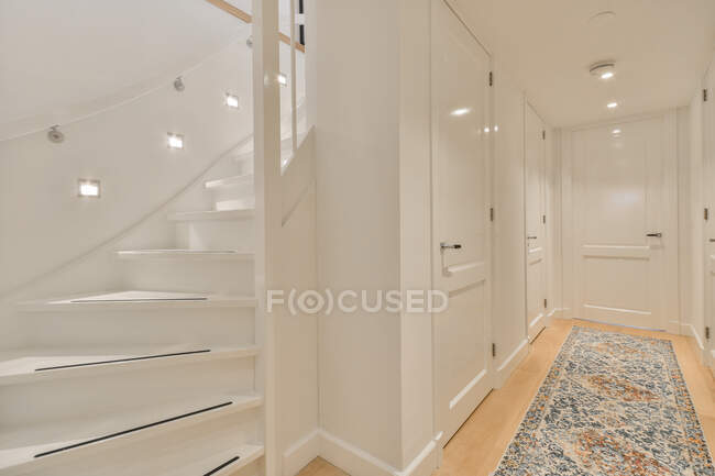 Interior blanco de pasillo estrecho y escalera iluminada por lámparas en casa contemporánea - foto de stock