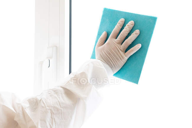 Männlicher Sanitäter in persönlicher Schutzausrüstung während der COVID-19-Pandemie im Krankenhaus beim Fensterputzen mit Lappen unkenntlich gemacht — Stockfoto