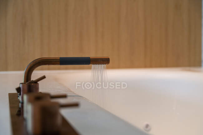 El agua que viene del grifo de cobre moderno en la bañera de cerámica en el baño minimalista con estilo - foto de stock