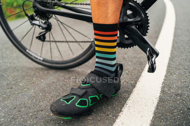 Наземний рівень безликого спортсмена в велосипедному взутті та смугастих шкарпетках, що стоять на проїжджій частині з велосипедом — стокове фото