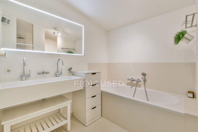 Creative design of bathroom with bathtub against cabinet and washbasin under mirror with lamp at home — Stock Photo