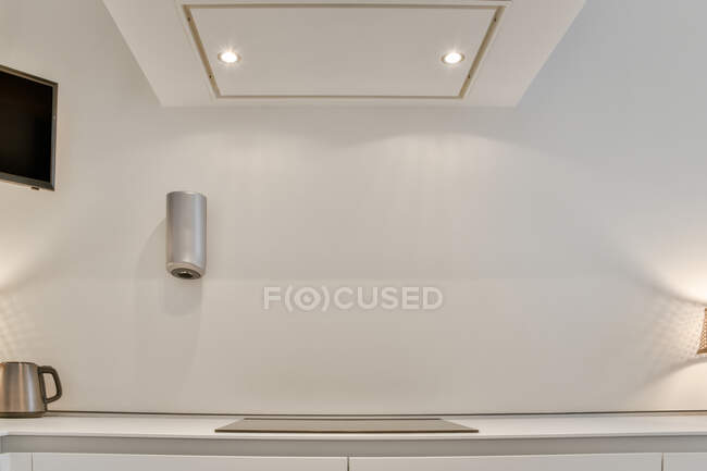 Interno cucina contemporanea con lampade sul cofano sopra piano cottura e bollitore sotto TV in casa — Foto stock
