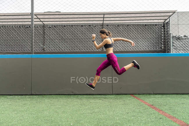 Full body of enduring female athlete in activewear jumping above ground during intense training in stadium — Stock Photo