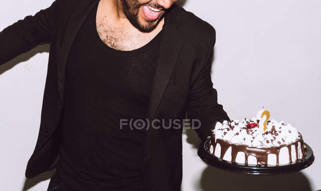 Crop cheerful male with mouth opened holding delicious birthday cake during party — Stock Photo