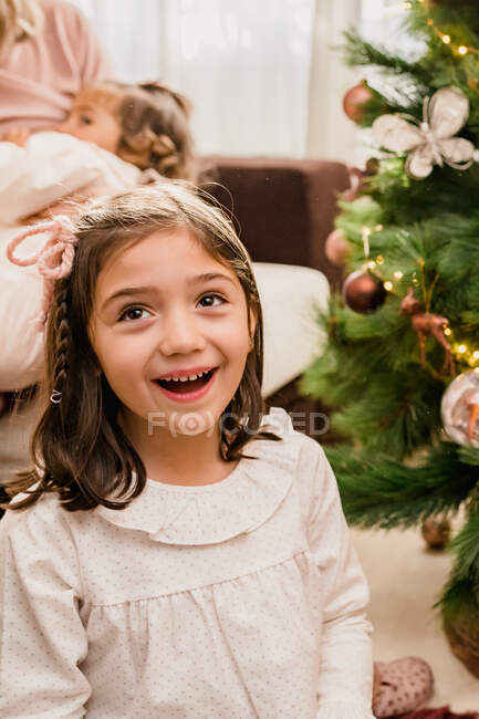 Pondering child looking up against crop anonymous mom breastfeeding baby during New Year holiday in house — Stock Photo
