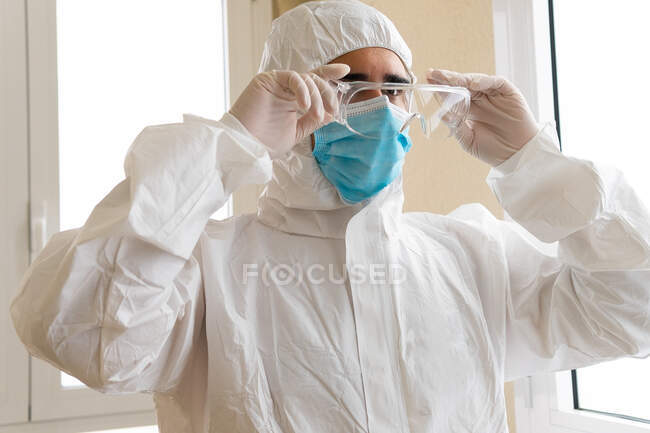 Adult male medic in personal protective equipment putting on goggles while looking forward in hospital — Stock Photo