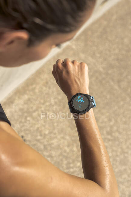 Desde arriba de la cosecha anónimo corredor femenino sudoroso comprobar el pulso en el rastreador de fitness durante el entrenamiento en el día soleado en verano - foto de stock