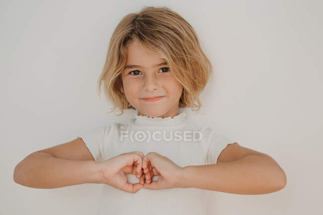 Enfant amical aux cheveux bruns montrant un geste d'amour avec les mains regardant la caméra — Photo de stock