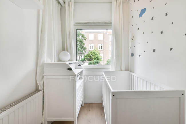 Culla in legno posizionata vicino alla finestra in camera da letto con interni minimalisti durante il giorno — Foto stock