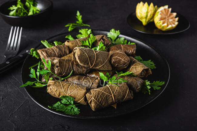 Palatable sarma with parsley lemon and fork and knife on dark background — Stock Photo