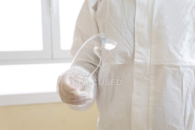Cropped unrecognizable male medic in personal protective equipment holding on goggles in hospital — Stock Photo