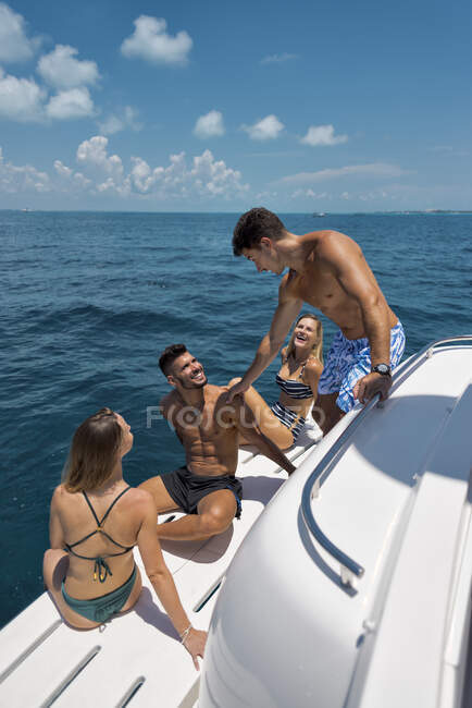 Молодой человек и женщина в купальниках наслаждаются летними каникулами с друзьями на яхте, плавающей в голубом океане в солнечный день — стоковое фото