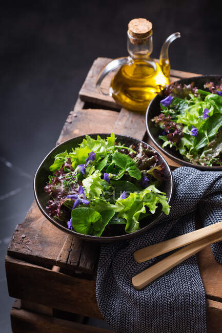 Dall'alto d'insalata vegetariana saporita con foglie di lattuga verdi e rosse e fiori commestibili contro brocca di olio — Foto stock