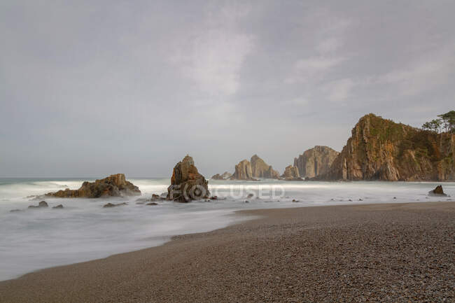 Espectacular paisaje con olas de mar espumosas lavando formaciones rocosas rugosas de diversas formas en la playa salvaje de Geirua en Asturias España - foto de stock