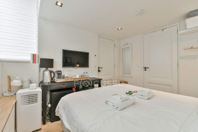 Design criativo de quarto com toalhas na cama contra mesa com bandeja sob televisão no hotel — Fotografia de Stock