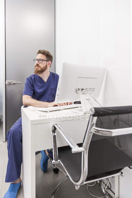 Homme en uniforme médical tapant sur le clavier de l'ordinateur tout en travaillant dans une clinique de soins de santé — Photo de stock