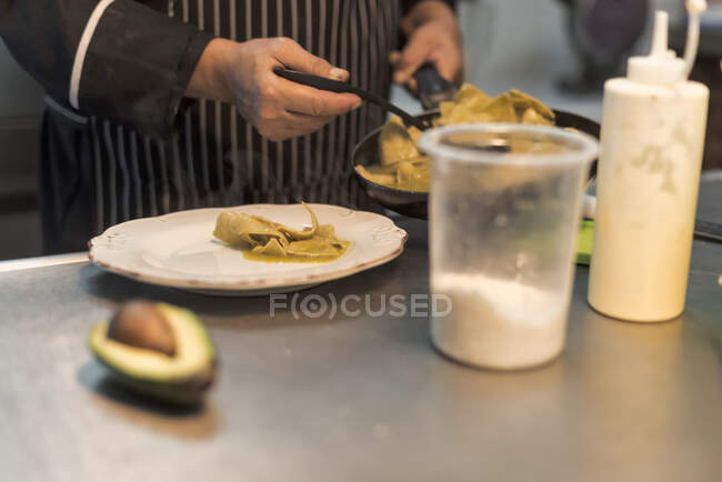Обрезанный неузнаваемый мужчина-повар, наливающий соус авокадо на приготовленную пасту на работе в ресторане — стоковое фото