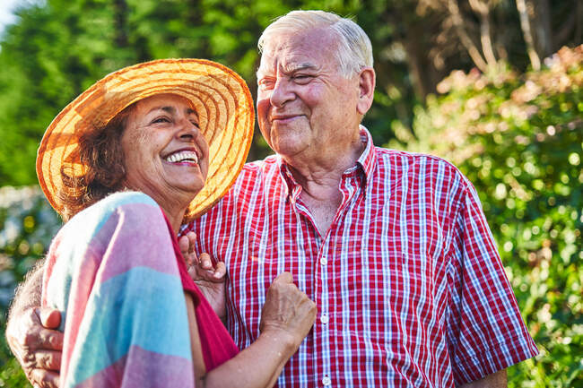 Gentle senior couple caressing looking away with tenderness while standing near shrubs in nature — Stock Photo