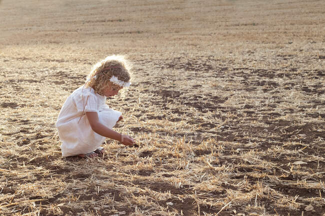 Vue de côté petite fille blonde seule dans un champ par une journée ensoleillée — Photo de stock