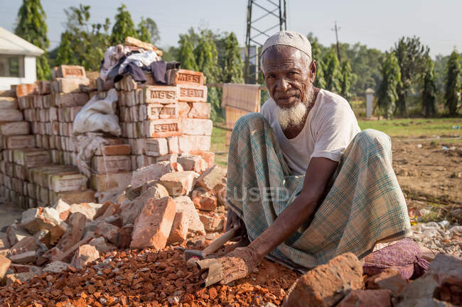 INDIEN, BANGLADESCHEN - 5. DEZEMBER 2015: Ethnische Männer in traditioneller Kleidung hocken in die Kamera, während sie in der Ziegelindustrie auf dem Land arbeiten — Stockfoto