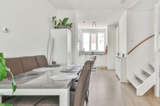 Table à manger vide et chaises placées dans une pièce lumineuse avec mobilier blanc dans un appartement contemporain en journée — Photo de stock