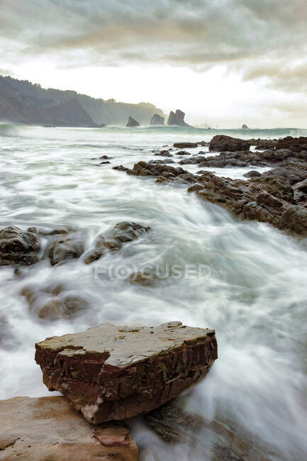 Cenário espetacular com ondas marinhas espumosas lavando formações rochosas ásperas de várias formas em Silence Beach, nas Astúrias Espanha — Fotografia de Stock