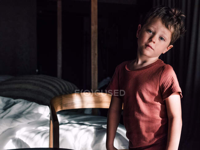 Liebenswertes kleines Kind, das neben dem Bett im gemütlichen Schlafzimmer steht und in die Kamera schaut — Stockfoto