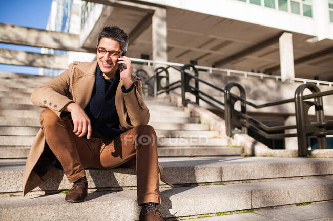 Joven con estilo en gafas y ropa casual sentado en las escaleras - foto de stock