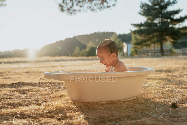 Kleinkind mit Spielzeug sitzt in Plastikwanne und spielt mit Wasser in der Natur — Stockfoto