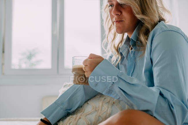 Vista laterale della femmina in camicia con tazza di caffè aromatico guardando lontano a casa — Foto stock