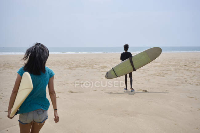 Vista posteriore di giovani surfiste multietniche con tavole da surf che parlano mentre passeggiano sulla riva sabbiosa e si guardano e si guardano — Foto stock