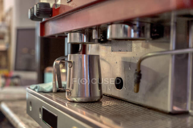 Metal pitcher on rack of professional coffee maker on table in cafeteria kitchen on blurred background — Stock Photo