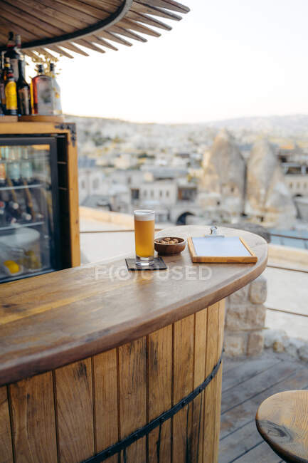 Bicchiere di birra fredda con snack e menù disposti su bancone rotondo in legno nel bar — Foto stock