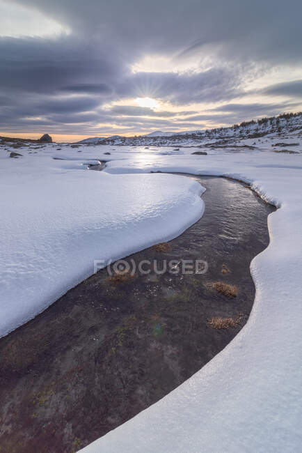 Landscape of snowy slope of hill in highland under cloudy sky in daylight and a river of ice water — Stock Photo