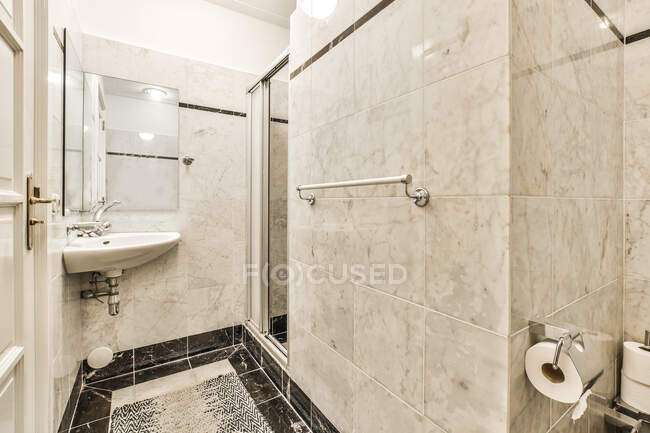 Интерьер современной светлой ванной комнаты с туалетом рядом с душевой кабиной и раковиной под зеркалом в современной квартире — стоковое фото