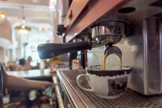 Anonyme Cafeteria-Mitarbeiterin gegen professionelle Kaffeemaschine, die Heißgetränk in Tasse auf verschwommenem Hintergrund gießt — Stockfoto