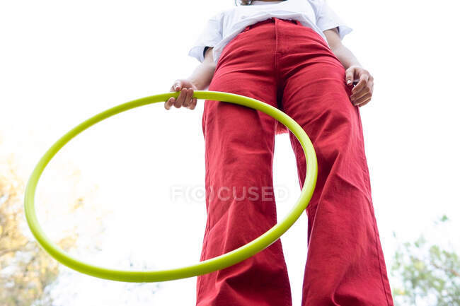 Dal basso del raccolto adolescente donna irriconoscibile in jeans rossi con hula hoop pur avendo tempo libero nel parco — Foto stock