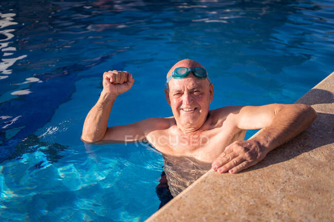 Angle élevé de l'homme âgé en maillot de bain avec poing levé nager dans la piscine bleue propre — Photo de stock