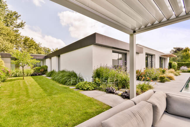 Prato erboso verde e piante tropicali nel cortile della casa moderna con accogliente zona salotto con comodi divani nella giornata di sole — Foto stock