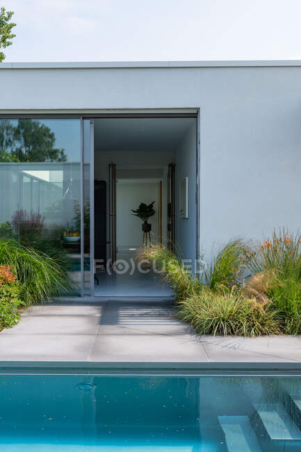 Swimming pool in yard of modern white villa with glass door on sunny day — Stock Photo