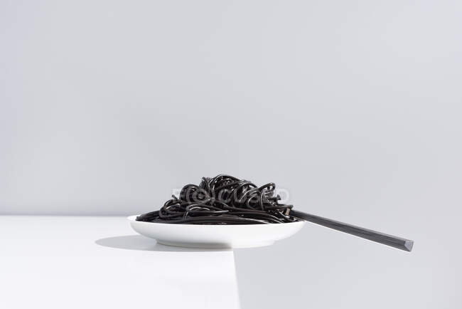 Forchetta inox in ciotola piena di spaghetti neri con inchiostro di seppia su tavolo bianco in studio su sfondo grigio — Foto stock