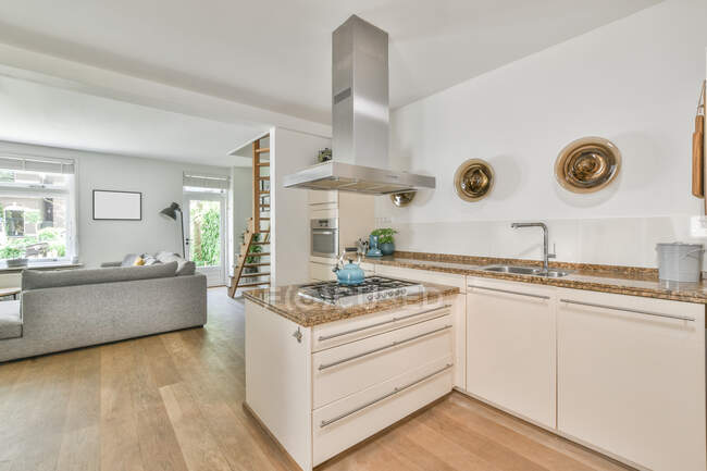 Bouilloire placée sur la cuisinière sous ventilation dans une cuisine spacieuse avec des meubles légers dans un appartement moderne — Photo de stock