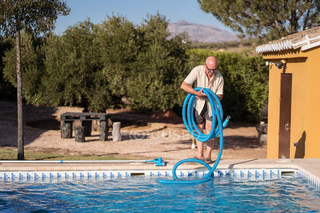 Full body of senior male in eyeglasses standing with rubber hose for swimming pool — Stock Photo