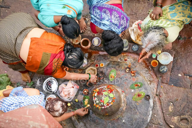 INDIA, VARANASI - NOVIEMBRE 2o, 2015: Desde arriba grupo de mujeres étnicas en mujeres asiáticas tradicionales en ropa tradicional india rezando y haciendo ofertas con velas y flores en la India - foto de stock