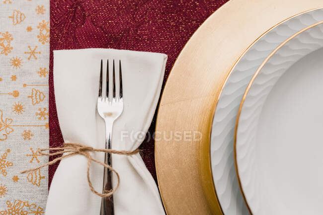 Top view of fork on napkin tied with thread placed near plated on served table for Christmas dinner — Stock Photo