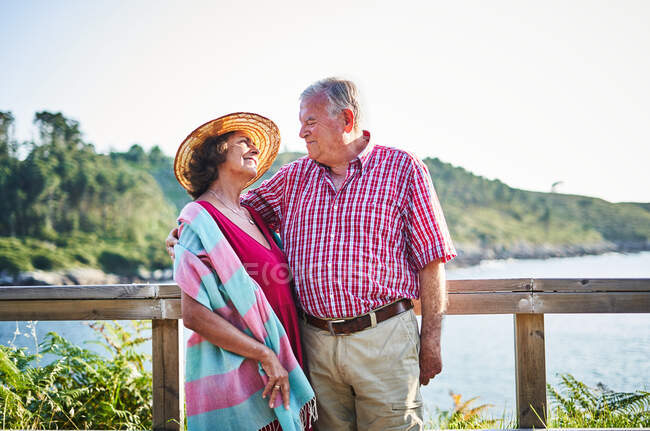 Seniorpaar steht dicht beieinander und schaut sich an und genießt den Blick auf das Meer an einem sonnigen Tag — Stockfoto