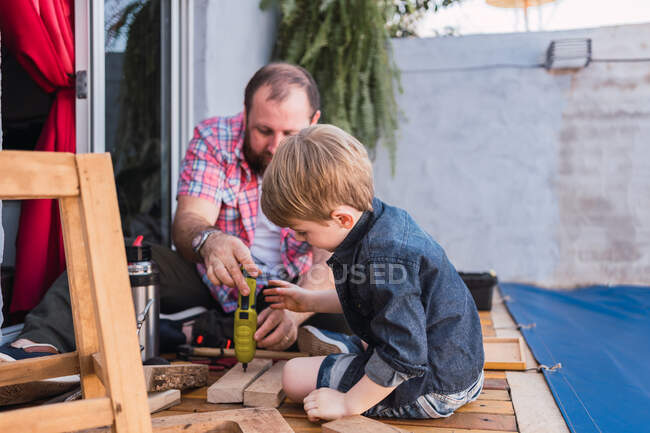 Unrasierter reifer Vater mit aufmerksamem Jungen, der Holzklötze mit Klebeband misst, während er Zeit auf verschwommenem Hintergrund verbringt — Stockfoto