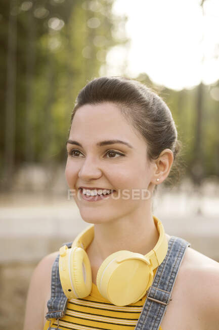 Mujer joven y positiva escuchando música en auriculares inalámbricos mirando hacia otro lado mientras camina por la calle - foto de stock