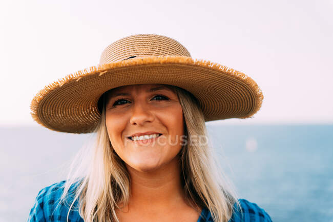 Portrait of cheerful adult female tourist in hat looking at camera against bright neutral background — Stock Photo