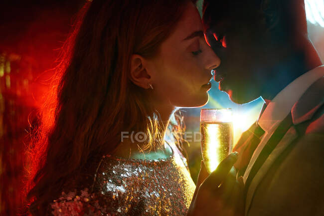 Seitenansicht des Erntepaares mit Glas auf Champagner im Moment des Kusses gegen glänzende Lichtstrahlen, die sich während der Party anschauen — Stockfoto